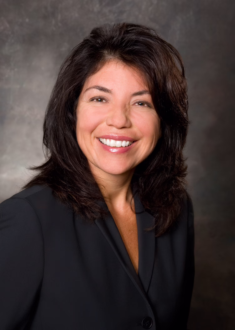 Smiling woman with dark hair in a black blazer, against a neutral background