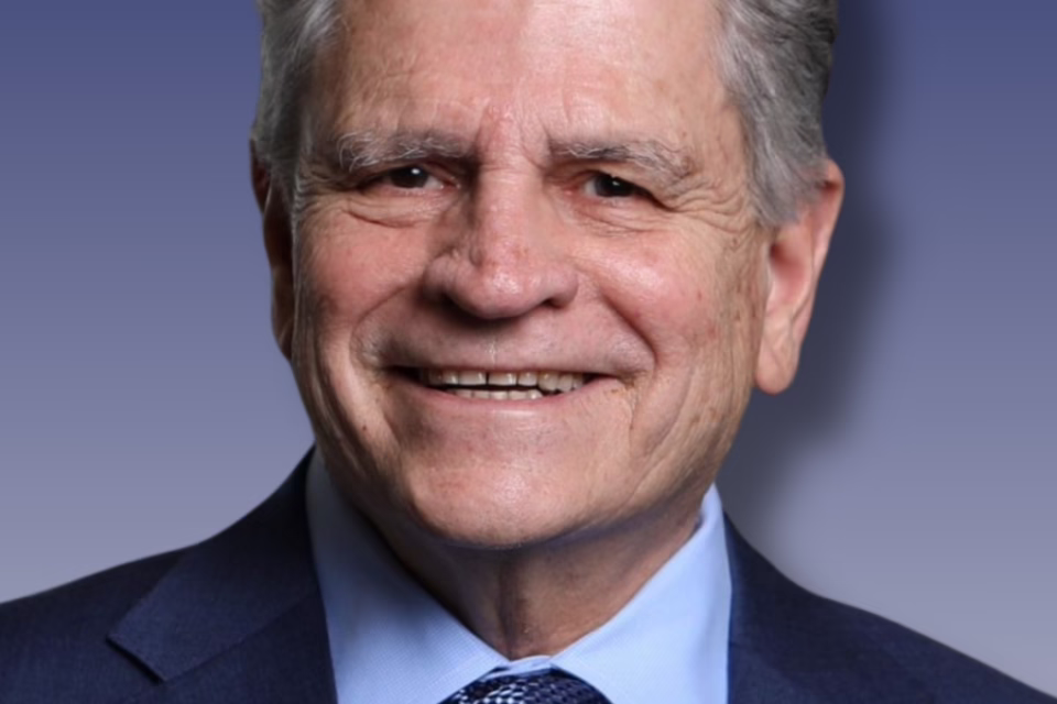 Smiling man in a suit with a blue tie against a gradient blue background