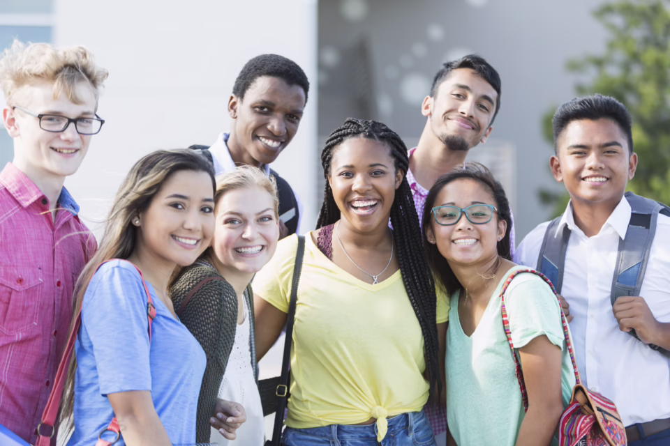 A diverse group of smiling students stands together outdoors, ready for the new school year