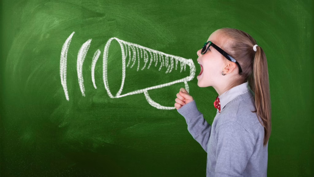 Child in glasses shouting into a chalk-drawn megaphone on a green chalkboard