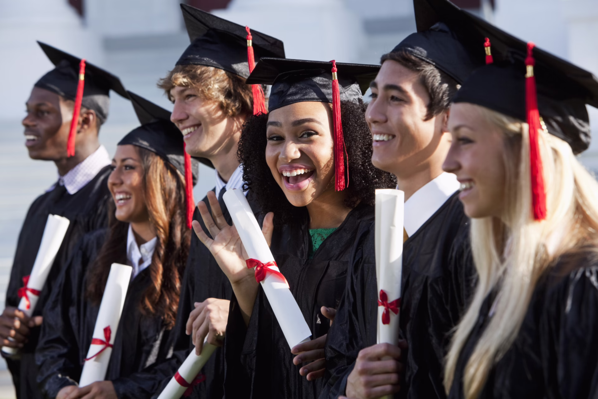 Graduates in caps and gowns hold diplomas, smiling and celebrating together