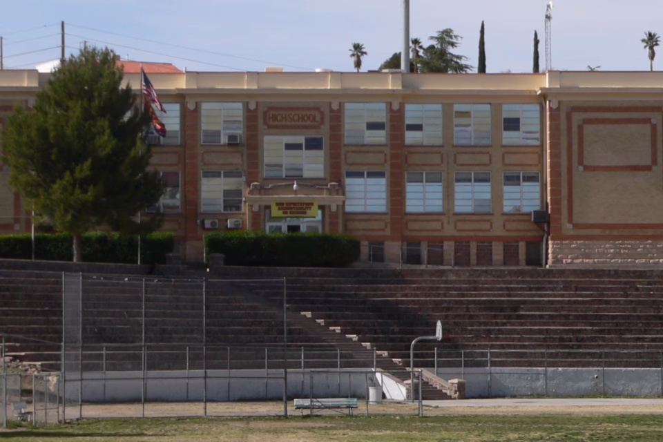 Front view of a high school building in Nogales, Arizona, with flags and a tiered seating area in front