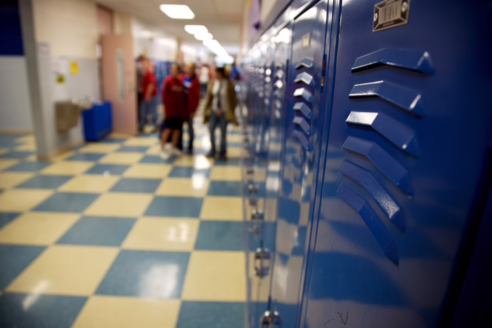 Blue lockers line a school hallway with a checkered floor. Students are blurred in the background
