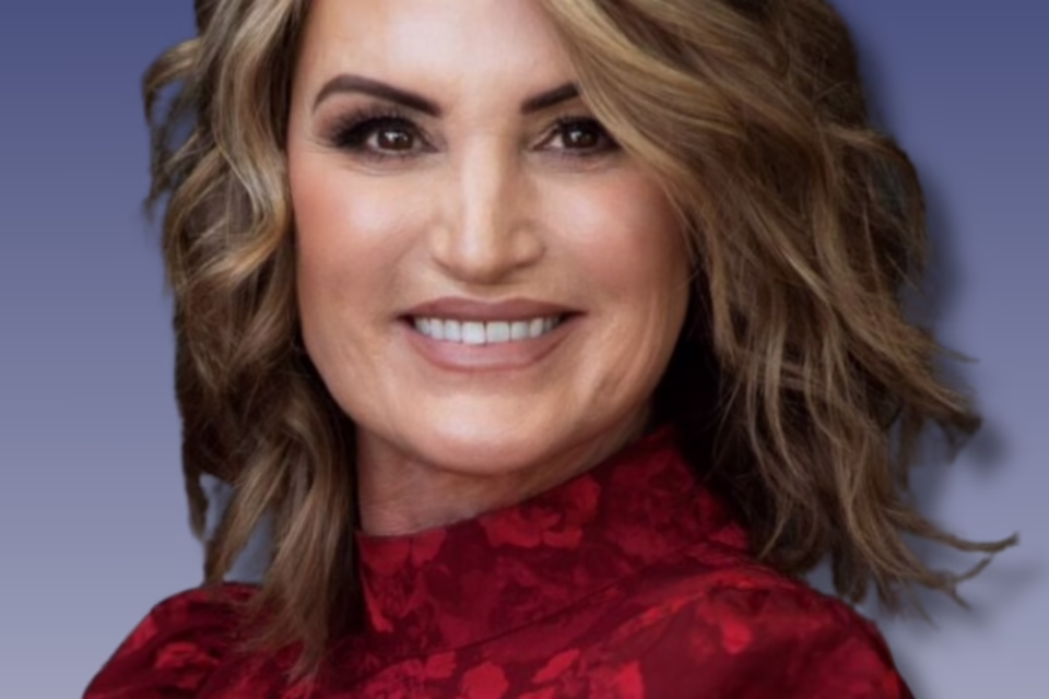 Smiling woman with wavy hair wearing a red floral blouse against a gradient blue background