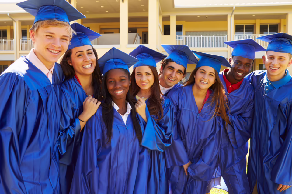 Group of diverse students in blue graduation gowns and caps smiling outdoors