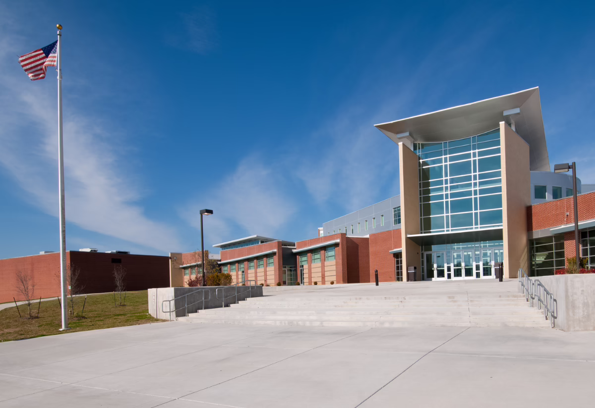 Modern school building with large windows, red brick exterior, and an American flagpole under a clear blue sky
