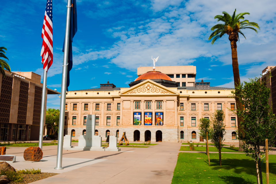 Arizona State Capitol building with American flag, palm trees, and clear sky