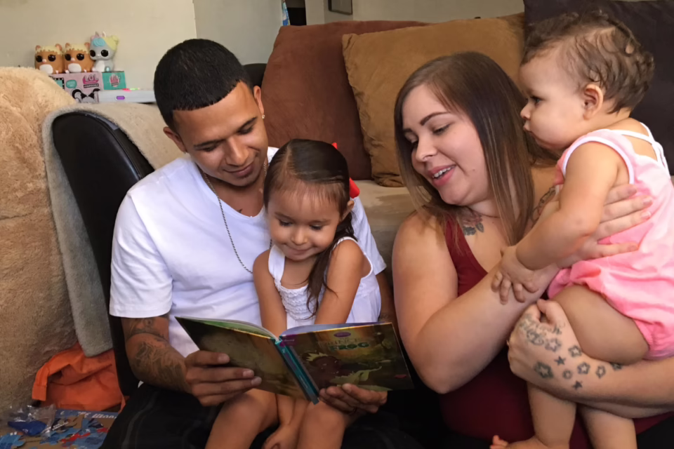 Family reading a book together on a couch, with toys in the background