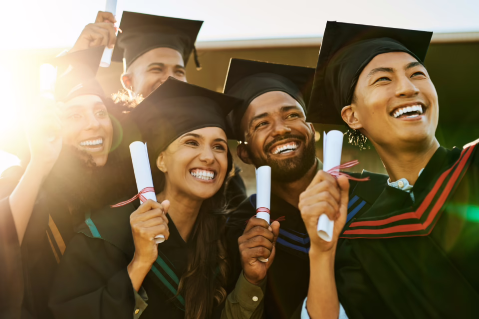 Graduates in caps and gowns holding diplomas, smiling in sunlight. Education Forward Arizona awards scholarships