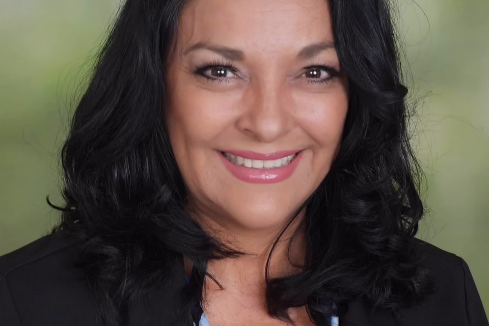 Smiling woman with dark hair in a blazer, against a blurred green background