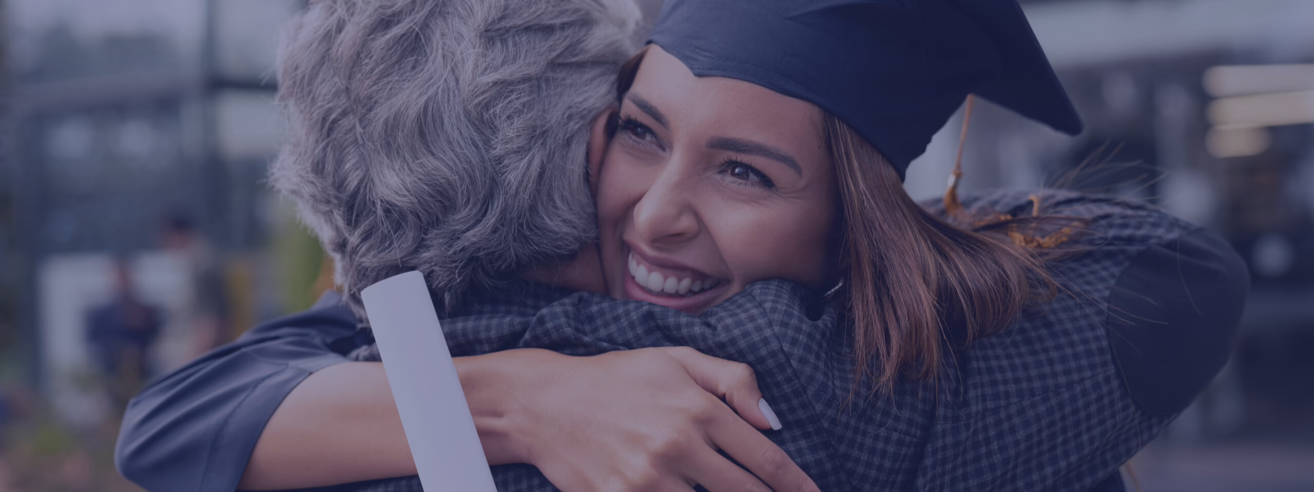 Graduate in cap and gown hugs an older person, smiling widely, holding a diploma