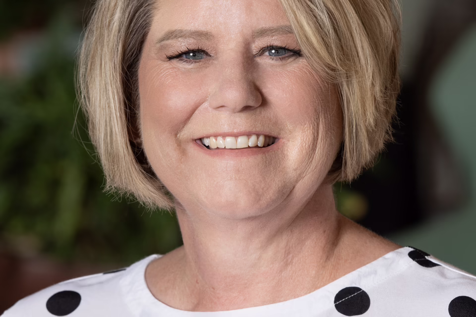 Smiling woman with short blonde hair wearing a white shirt with black polka dots