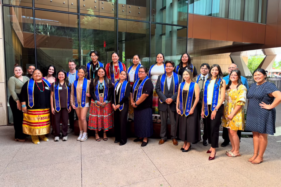 Group of Arizona graduates wearing blue stoles, standing outside a modern building, celebrating the Class of 2025