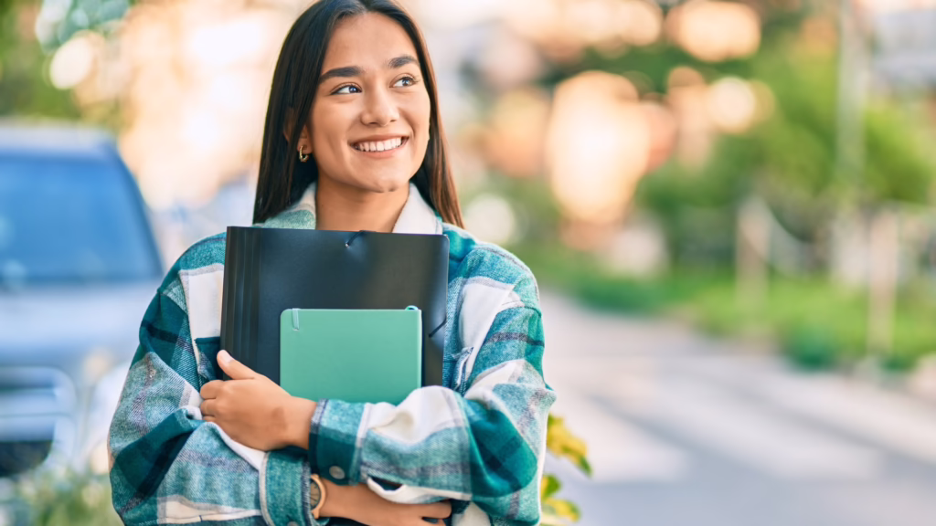 Smiling student holding binders outdoors